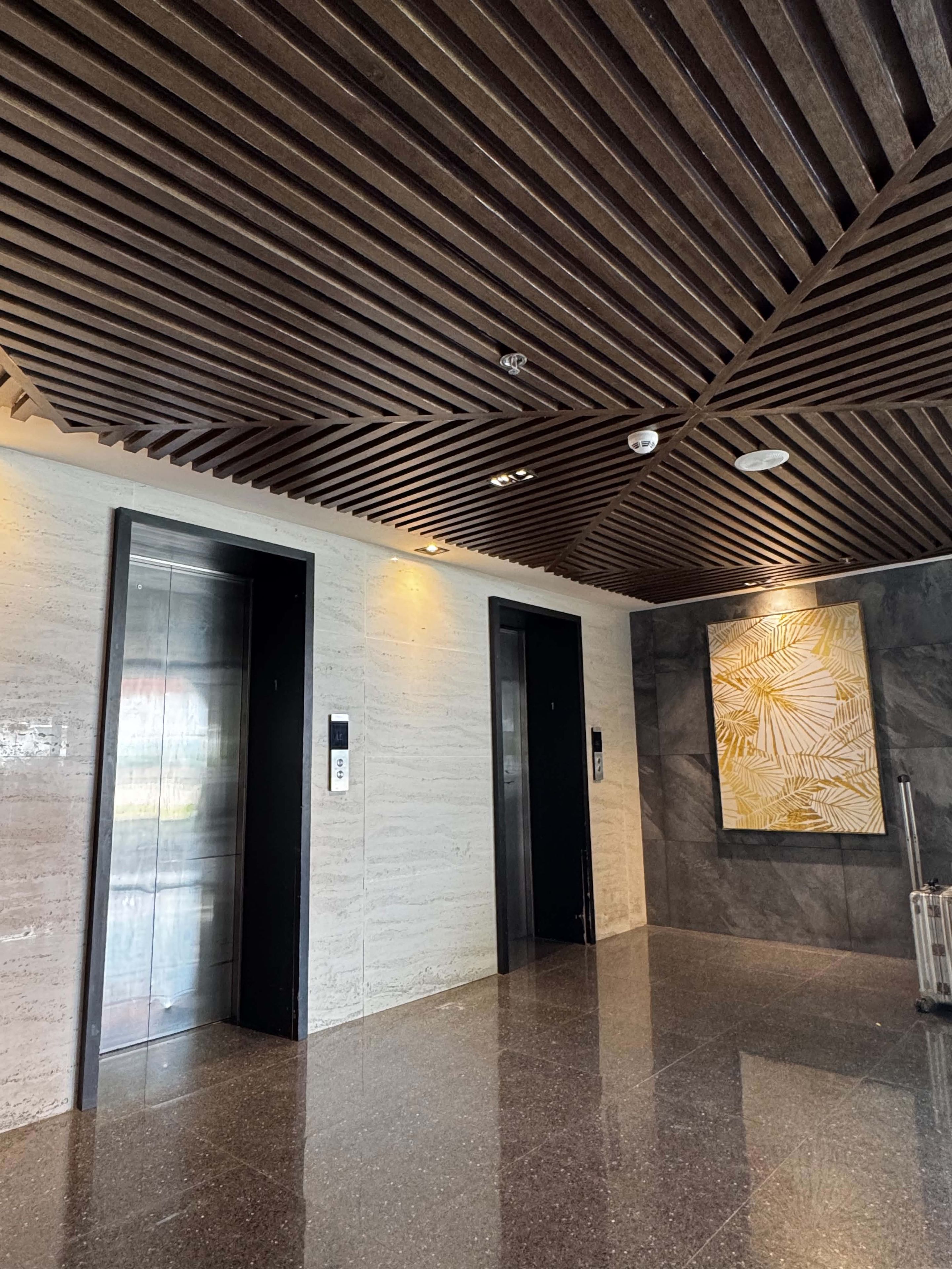 Interior moderno com dois elevadores, piso polido e parede com padrão geométrico.