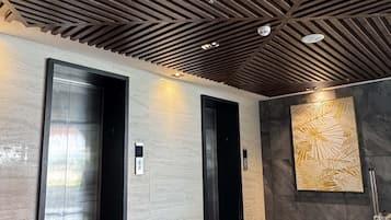Interior moderno com dois elevadores, piso polido e parede com padrão geométrico.