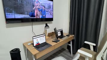 Um espaço de escritório em casa com uma mesa, dois notebooks, um computador de mesa, uma televisão e uma cadeira.