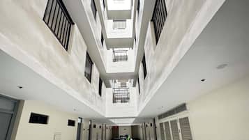 Um corredor com um caminho central, ladeado por paredes com janelas e portas, que leva a um teto alto com claraboia.
