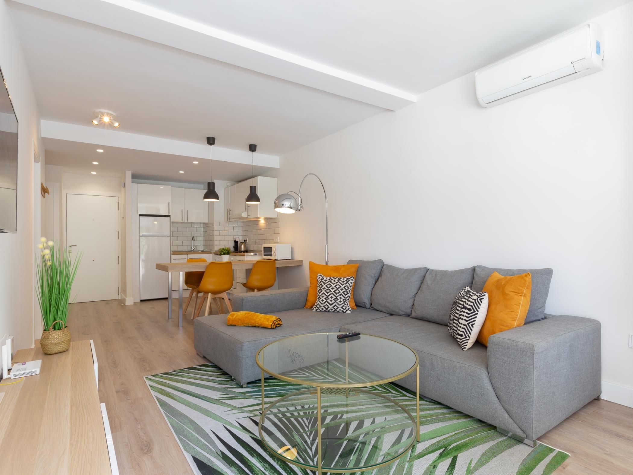 Ein modernes Wohnzimmer mit einem grauen Sofa, einem Glastisch und einem Essbereich mit gelben Stühlen.