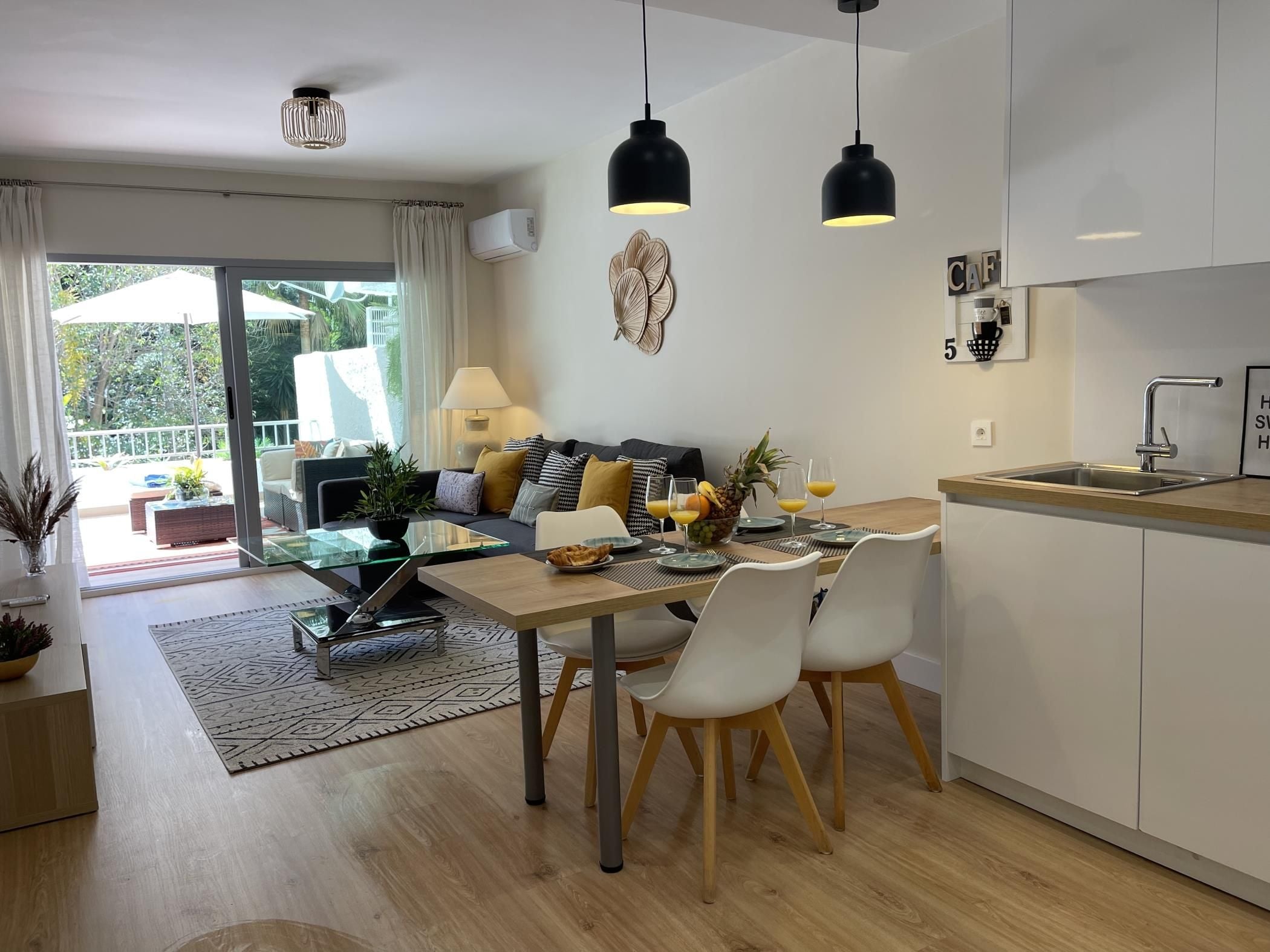 A modern kitchen with a dining area, a sofa, and a view to the outside.