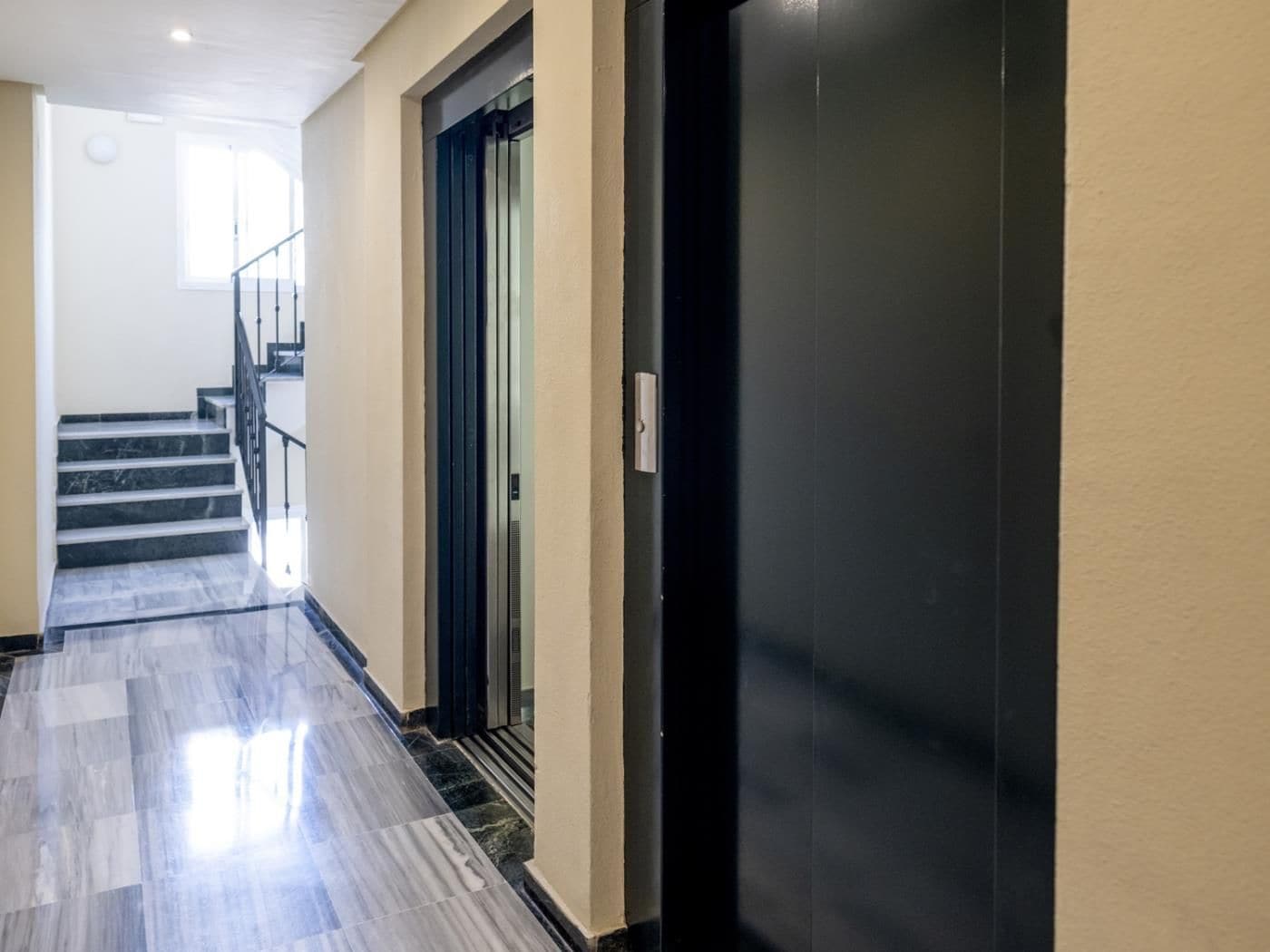 A hallway with a staircase, a door, and a light fixture on the wall.