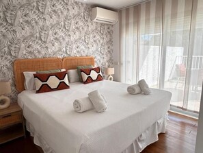 A hotel room with a large bed, a headboard with a leaf pattern, and a view of the outdoors through a window. - Gardens of the Sea 332 (Marbella)