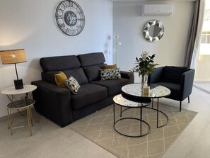 A modern living room with a dark sofa, a round coffee table, and a decorative clock on the wall. - Beachfront duplex1 Bedroom Marbella (Marbella)