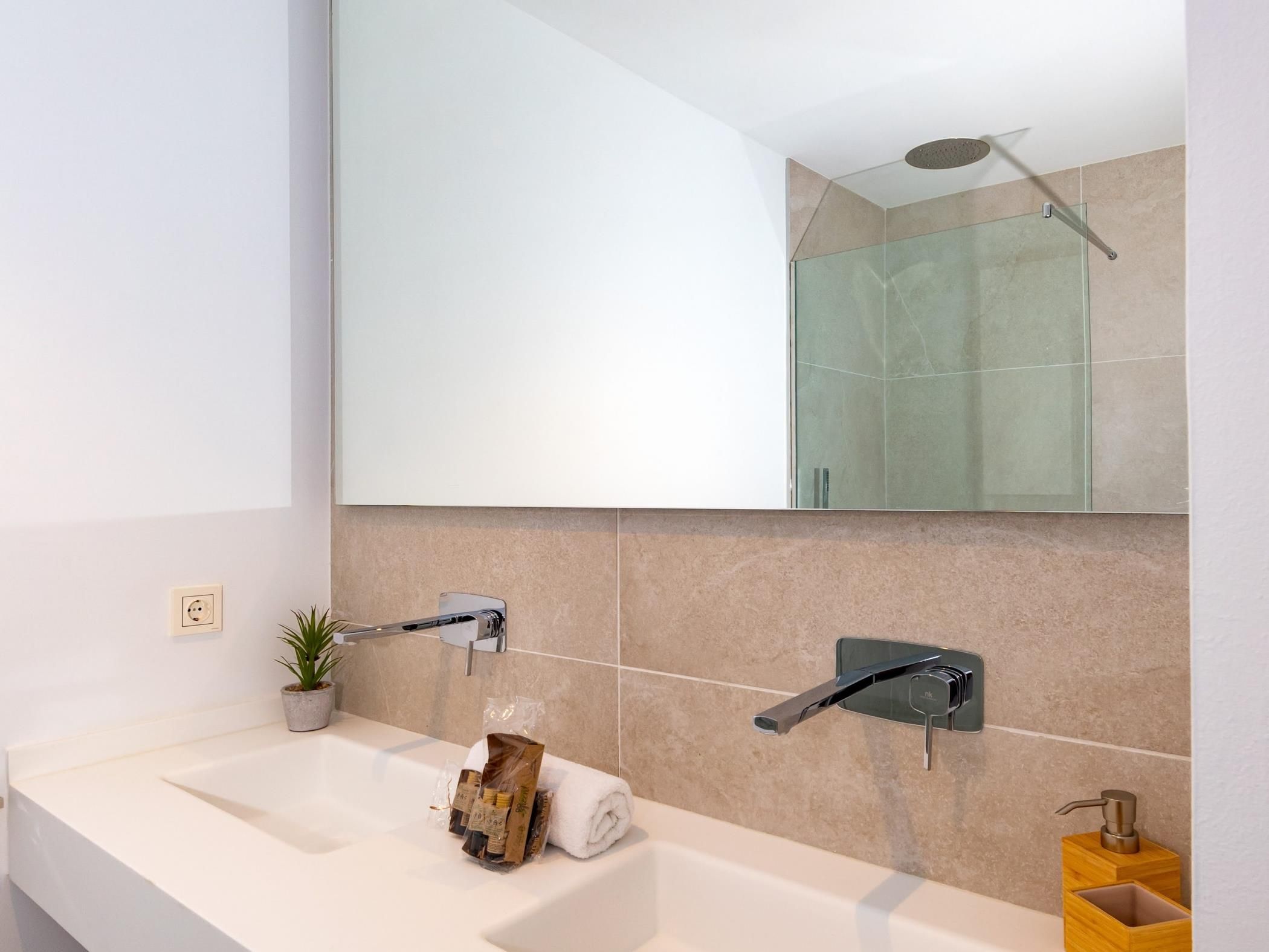 Ein modernes Badezimmer mit einem großen Spiegel, einem Waschbecken und einer Dusche.