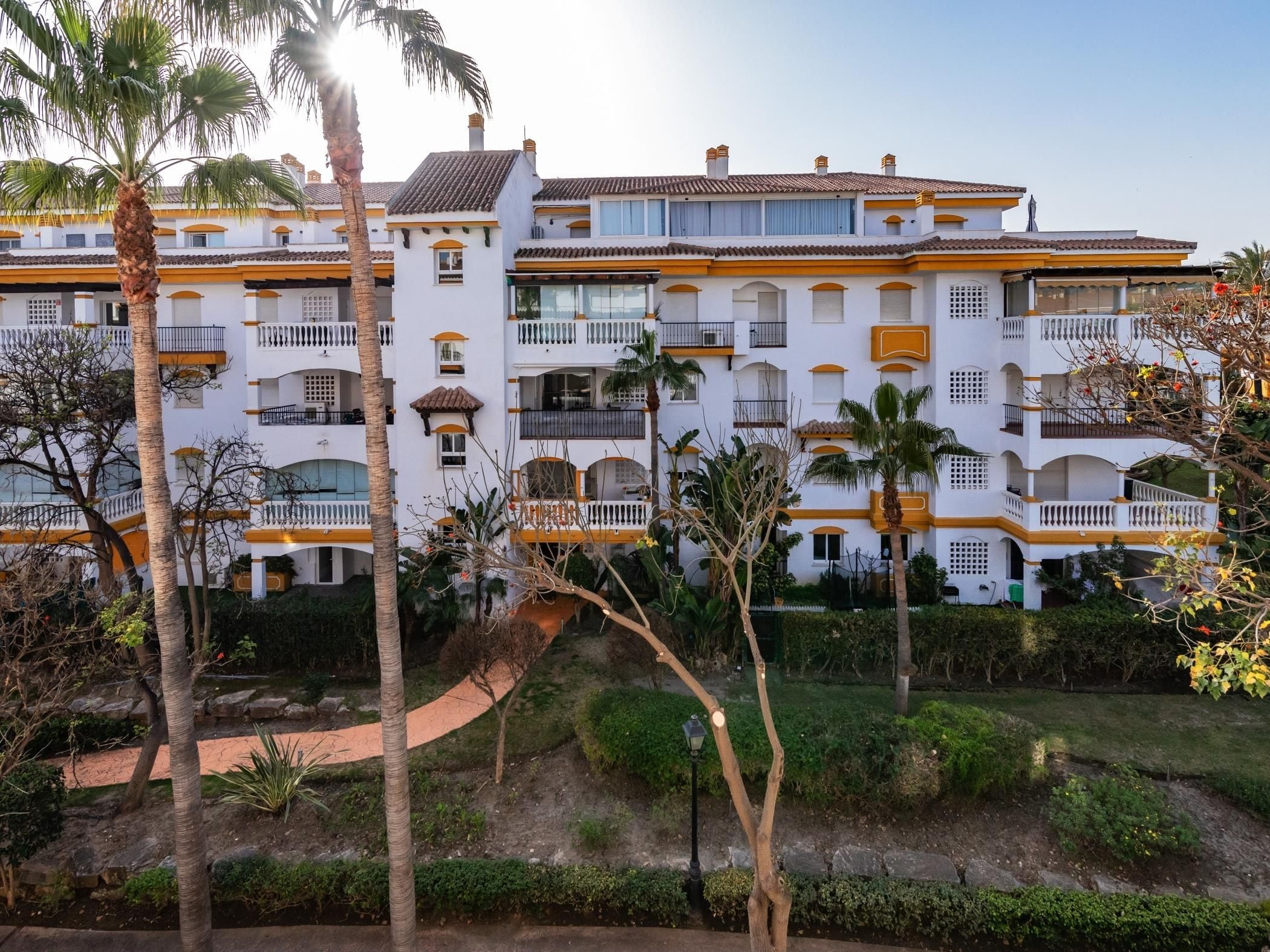 A multi-story hotel with balconies, palm trees, and a well-maintained garden.
