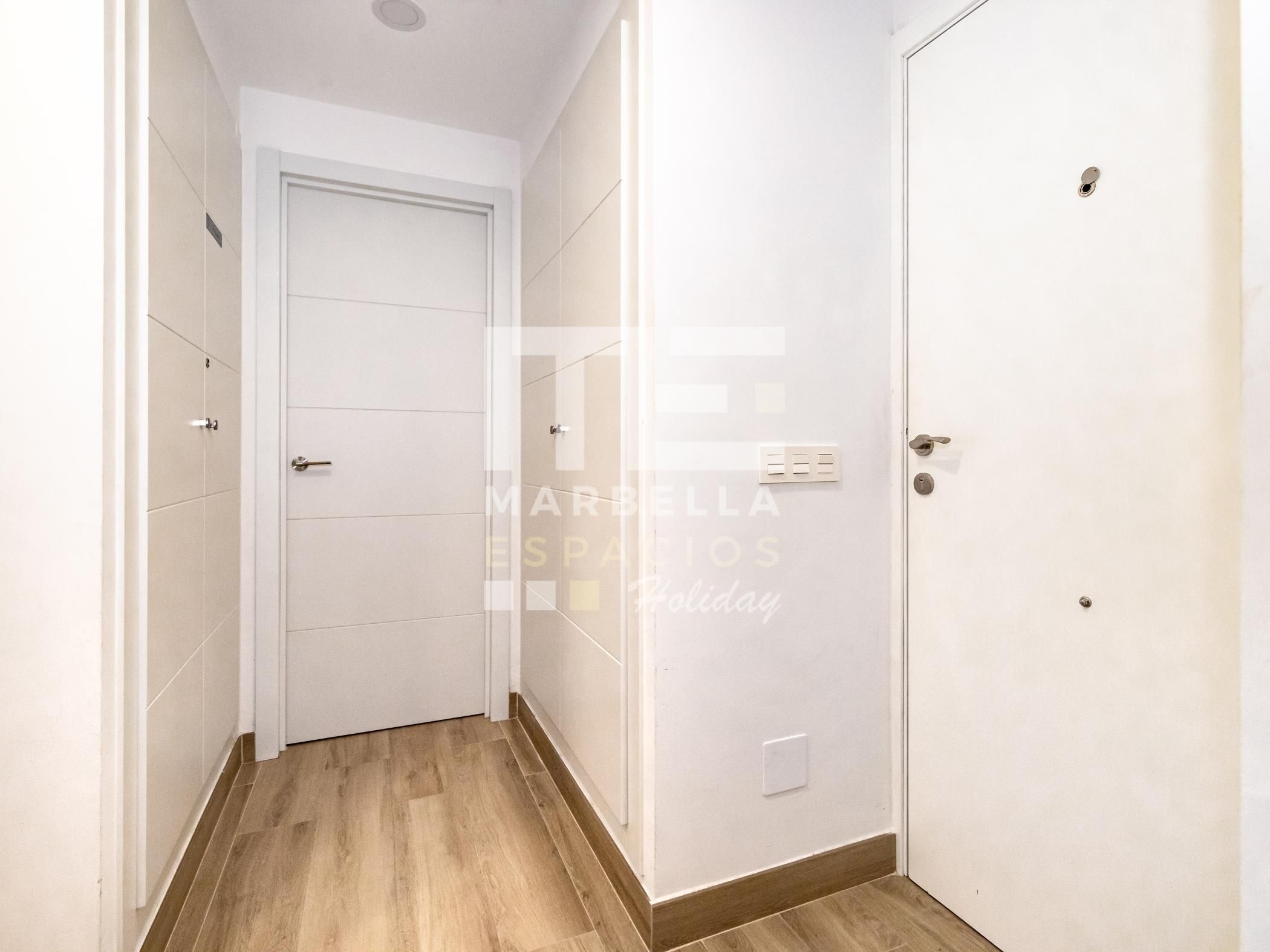 Un couloir étroit avec un plancher en bois, des murs blancs et une porte fermée au bout.