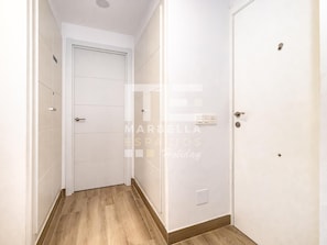Un couloir étroit avec un plancher en bois, des murs blancs et une porte fermée au bout.
