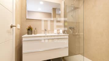 Une salle de bain moderne avec une douche à parois de verre, un meuble-lavabo blanc avec un miroir et deux paniers placés sous le plan de travail.