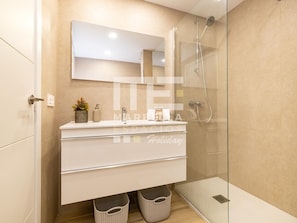 Une salle de bain moderne avec une douche à parois de verre, un meuble-lavabo blanc avec un miroir et deux paniers placés sous le plan de travail.