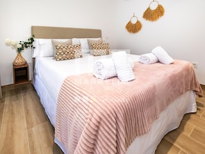 Un lit bien fait, avec une couverture rose, des oreillers blancs et un vase rempli de fleurs posé sur une table de chevet.