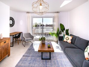 A modern living room with a sofa, a coffee table, a chair, and a dining table. There is a balcony with a view of the city. - El Dorado 3 bedrooms near Puerto Banus (Marbella)