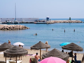 A beach with thatched umbrellas, a rocky breakwater, and boats in the background. - El Dorado 3 bedrooms near Puerto Banus (Marbella)
