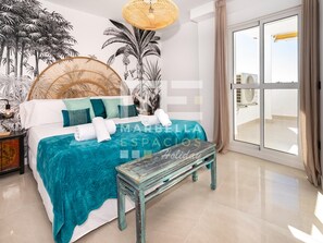 A bedroom with a bed, pillows, a bench, a wall-mounted lamp, and a large window. - El Dorado 3 bedrooms near Puerto Banus (Marbella)