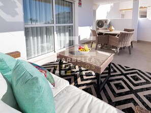 A balcony with a sofa, a table with fruit, wicker chairs, and a large window. - El Dorado 3 bedrooms near Puerto Banus (Marbella)