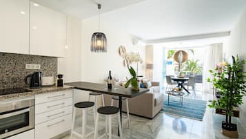 Eine moderne Küche mit Marmorarbeitsplatte, weißen Schränken und einem Essbereich mit einer Couch und Barhocker.