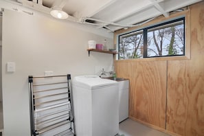 A compact laundry room with a washing machine, a drying rack, and a window with a view of trees. - Parapara Escape Beach House (Takaka)