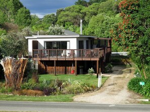 A two-story house with a balcony, surrounded by lush greenery and a dirt path leading to the entrance. - Parapara Escape Beach House (Takaka)