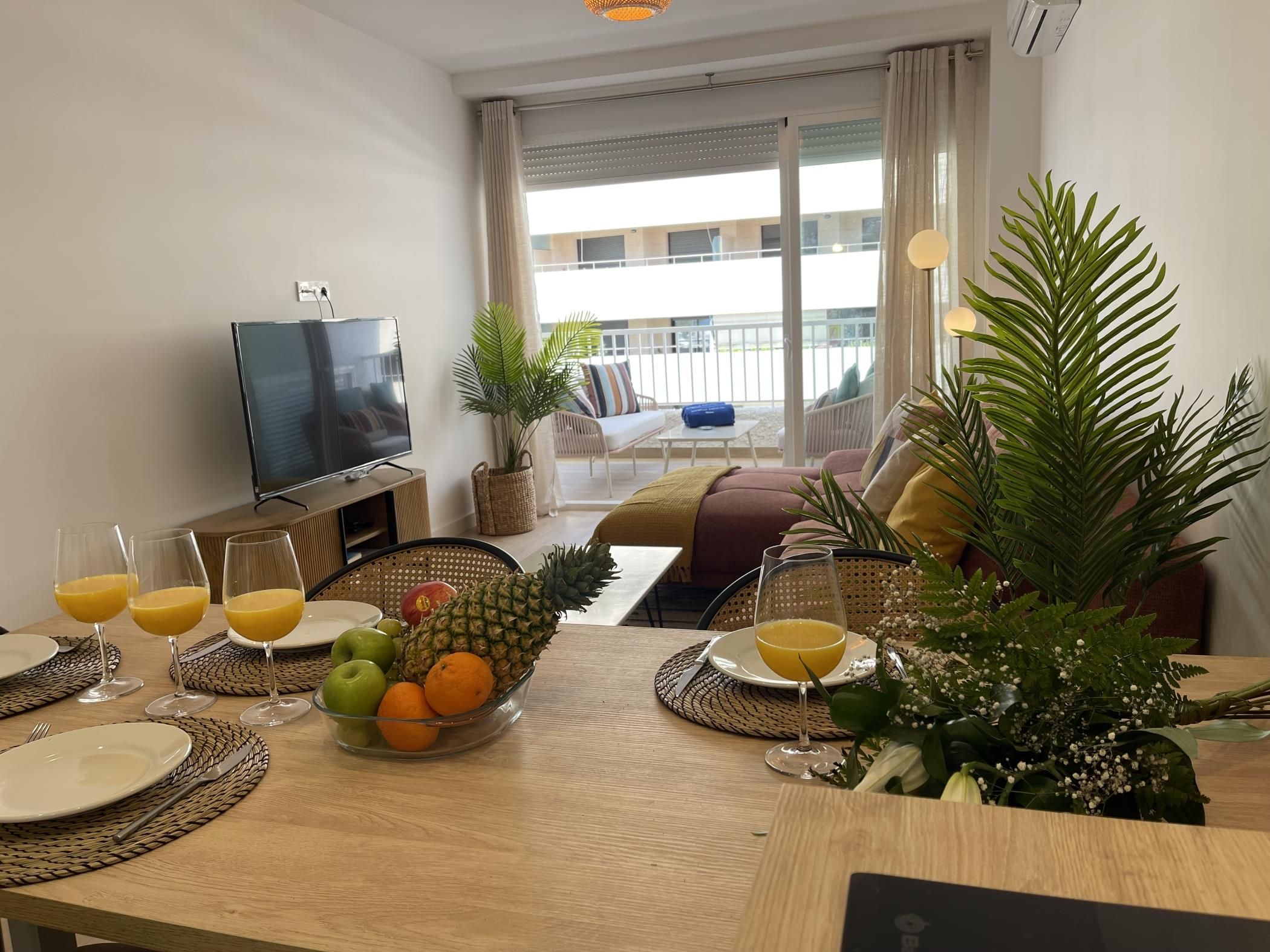 A modern living room with a television, seating area, and a dining table set with fruit and drinks.