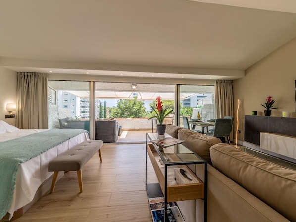 Une chambre d’hôtel avec un lit, un canapé, une petite table, une télévision et un balcon donnant sur des immeubles et des arbres.
