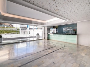 Un hall d’hôtel moderne avec une façade en verre, un comptoir d’accueil et un sol décoré d’un motif en chevrons.