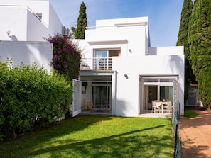 A modern white house with a covered patio, a small garden, and a tall tree.