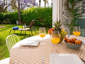 An outdoor dining area with a checkered tablecloth, a fruit bowl, croissants, and glasses of orange juice.