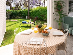 An outdoor dining area with a checkered tablecloth, a bowl of fruit, and a bottle of water.