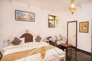 A hotel room with a bed, a nightstand, a sofa, a door, and a wall-mounted picture. - Vikramgarh Lakeview- A Royal Collection (Udaipur)