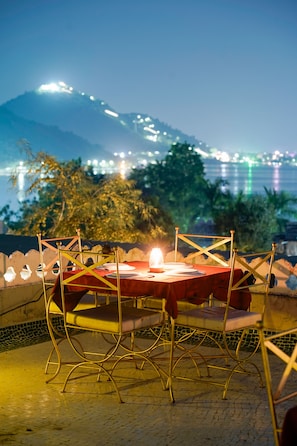 An outdoor dining area with a table set for two, chairs, and a candle. - Vikramgarh Lakeview- A Royal Collection (Udaipur)