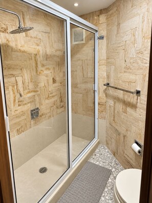 A modern bathroom with a glass shower enclosure, wooden wall paneling, a toilet, and a towel rack. - Beautiful Oceanfront Suite in the Heart of Acapulco (Acapulco de Juárez)