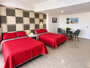 Quarto de hotel com duas camas, uma escrivaninha, cadeiras e obras de arte na parede.