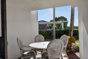 Eine Terrasse im Freien mit einem runden Tisch und Korbstühlen, mit Blick auf einen Garten mit einer Pergola und einem Haus im Hintergrund.
