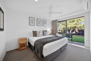 Una camera da letto con un letto, un ventilatore a soffitto e vista su un giardino tramite una porta scorrevole.