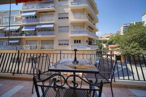Un balcon avec une table et des chaises, une clôture en métal et, au fond, un immeuble à plusieurs étages doté de balcons.