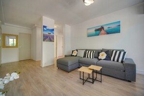 Un salon moderne avec un canapé d’angle gris, une petite table en bois et deux tableaux accrochés au mur.