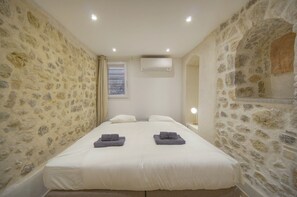 Ein Schlafzimmer mit Steinwänden, einem Bett mit weißer Bettwäsche, zwei Kissen und einem Fenster mit Vorhängen.