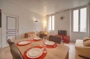 Ein Essbereich mit einem Tisch für vier Personen, einer Couch, einem Fernseher und einem Fenster mit Vorhängen.