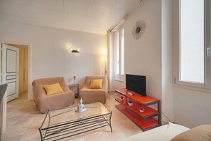 A living room with two sofas, a coffee table, a TV on a red stand, and a wall clock. - Frgk Clemenceau 1-Bedroom Beach Apartment with UltraFast Wi-Fi (Cannes)
