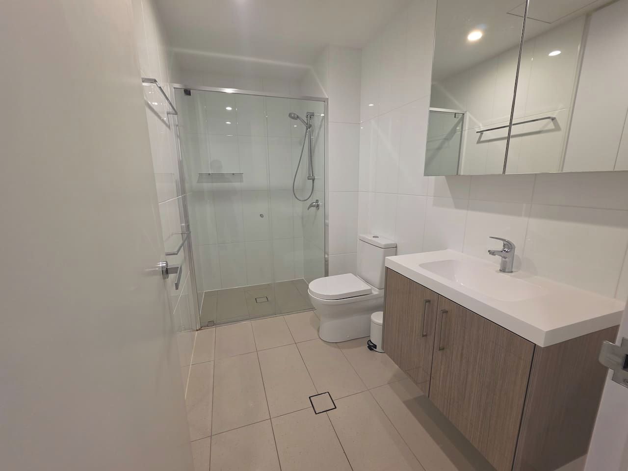 Une salle de bain moderne avec une douche à parois de verre, des toilettes blanches et un meuble-lavabo en bois avec un évier.