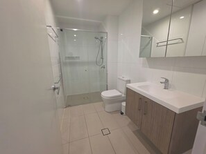 Ett modernt badrum med en dusch som är avskärmad med glasv äggar, en vit toalett och ett handfat med underskåp i trä.