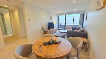 Een moderne woonkamer met een ronde houten tafel, twee fauteuils, een bank en een televisie.