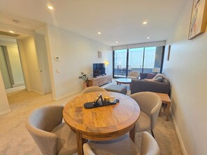Een moderne woonkamer met een ronde houten tafel, twee fauteuils, een bank en een televisie.
