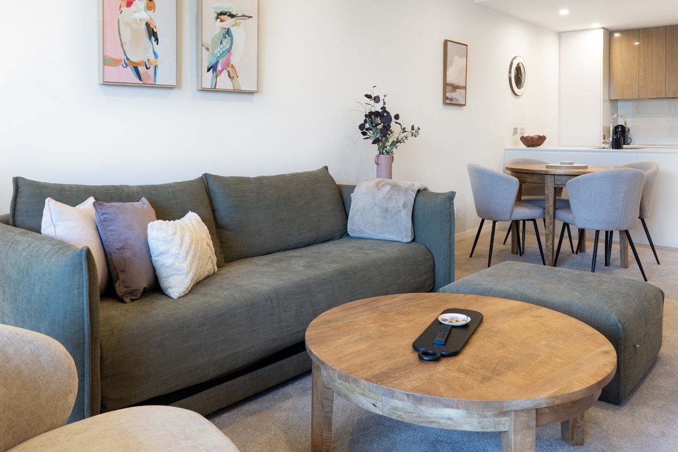A modern living room with a grey sofa, a round wooden coffee table, and a dining area with grey chairs and a wooden table.