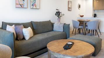 A modern living room with a grey sofa, a round wooden coffee table, and a dining area with grey chairs and a wooden table.