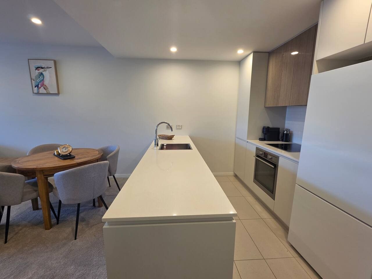 Uma cozinha moderna com uma ilha central, mesa de jantar com cadeiras e forno embutido.