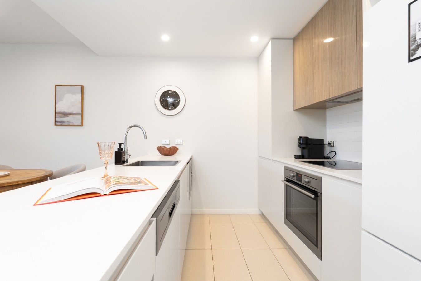 A modern kitchen with white cabinetry, a built-in oven, and a wall-mounted clock.