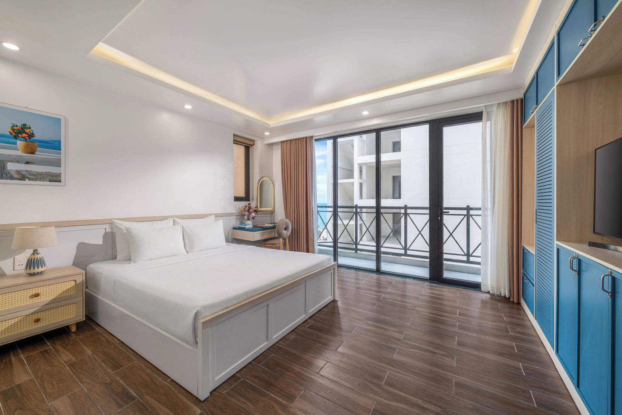 A hotel room with a large bed, a bedside table, a TV, and a balcony with a view.