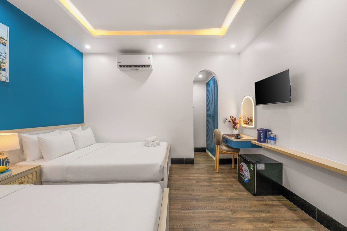 A hotel room with two beds, a desk with a computer, a TV, and an air conditioning unit.
